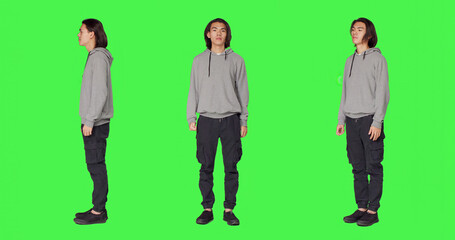 Obraz premium Proud person standing in studio and posing with confidence, acting joyful against full body green screen backdrop, with young smiling man being optimistic and friendly in casual clothes.