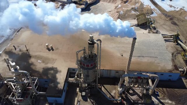 Aerial view of an industrial forestry complex with wood chip piles, drying infrastructure, handling equipment, and a prominent steam plume.