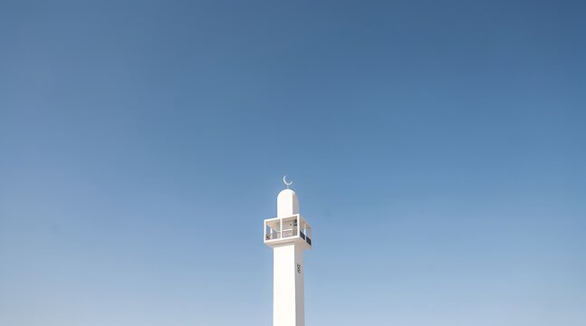 A tall, slender white minaret with a crescent moon on top stands against a clear, bright blue sky.