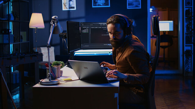 Developer typing code in home office, using Java programming language to develop software application, IT professional using multimonitor PC setup and laptop to finish tasks.