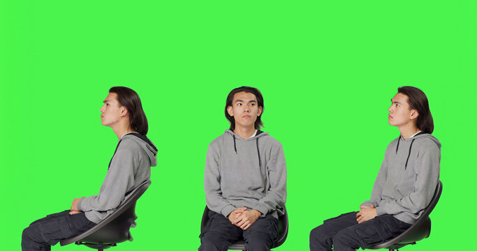 Young man checking wristwatch and waiting in studio, acting impatient while sitting on chair over green screen, male model looking at time on camera, optimistic person with watch.