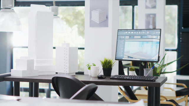 Designing office has empty desk with computer operating CAD, production layouts and blueprints on the design table, architectural work environment fitted with latest modeling appliances.