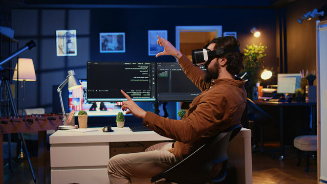 Remote software developer using VR goggles in personal office at home to do JavaScript programming, IT engineer wearing virtual reality headset in order to visualize lines of code.