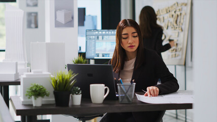Asian engineer constructing residential plans using CAD program, working on laptop with manufacturing tools and industrial scale specifications, developer illustrating a design idea, handheld shot. © DC Studio
