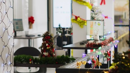 Obraz premium Empty festive ornate office with Christmas lights and red bows on walls. Financial graphs on computer screens in xmas adorn workplace with no company personnel during winter holiday season