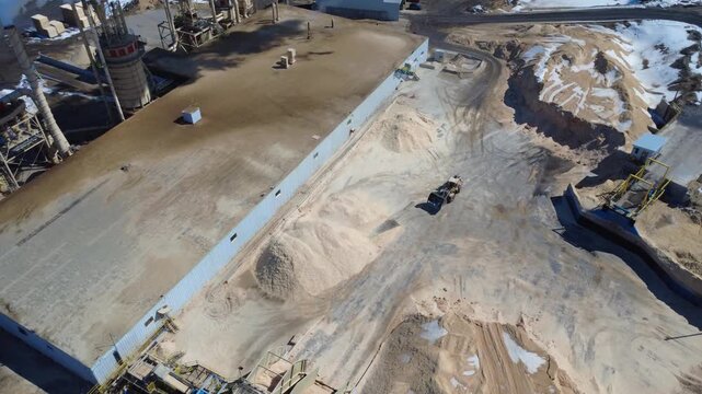 Drone footage of a wheel loader moving wood chips at a large industrial wood processing complex with conveyors, filtration systems, and storage areas.