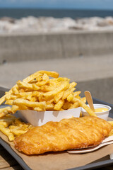 Fototapeta premium Fish and chips on Le Treport promenade golden battered cod with mountain of french fries, seaside flavors enjoyed outdoors by the harbor in Normandy, France