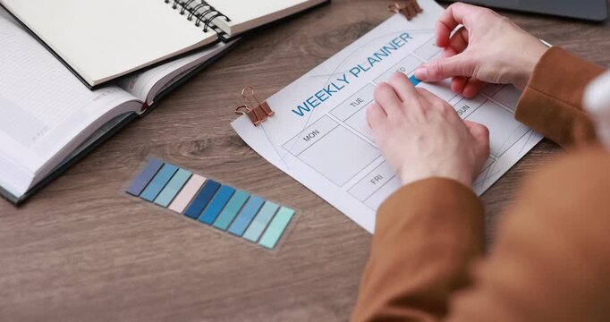 Woman putting sticker on weekly planner at wooden desk, closeup