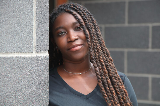 Calm young Black woman with long braids leaning against a gray urban concrete wall