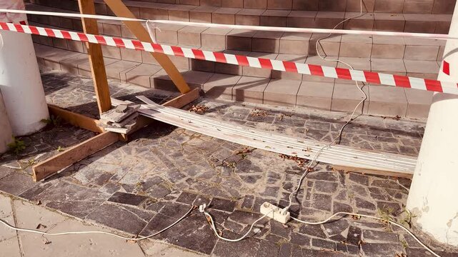 Sunlit low-angle exterior showing a building entrance being renovated, featuring wooden stair risers, temporary bracing, red-and-white safety tape