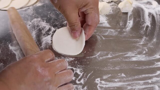 Close up of human hands using a wooden rolling pin to flatten a dough wrapper for Chinese dumplings