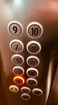 Close-up of an elevator control panel showing numbered buttons. The button for the 1st floor is illuminated in red. The panel has a sleek metallic finish