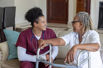 Naklejka premium Male nurse and Senior African-American woman sitting on couch holding walker and stethoscope