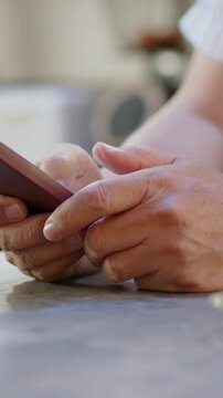 Vertical video: Thumb hovering hands tapping and swiping phone at countertop pink case short sleeve