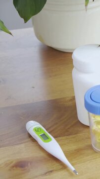 Vertical video: Panning cam revealing thermometer on wood table opening view to plant pot and pills