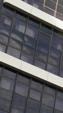 Vertical video: Camera panning upward at urban facade, showcasing glass panels, balconies, vent