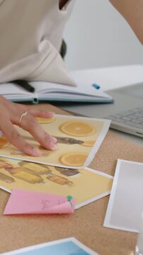 Vertical video: Smoothing hand in light top laying prints on corkboard, placing bottles for layout