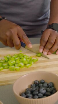 Vertical video: Placing stalk, hands slicing with blue knife on board at counter for salad, berries