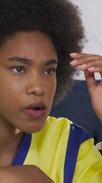 Vertical video: Fan in yellow kit holding soccer ball, reacting to play in stands and rubbing head