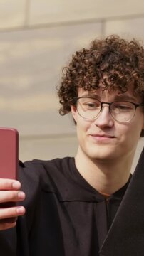 Vertical video: Holding red phone, grad in hoodie reacting to graduation at wall, holding black cap