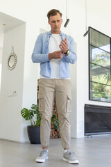 Obraz premium Man standing adjusting wristwatch in modern living area, wearing blue shirt and beige cargo pants