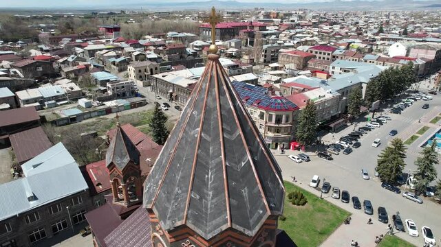 An aerial drone shot of the historic Holy Saviour Church in Gyumri, Armenia, showcasing its unique black tufa stone architecture and the surrounding cityscape on a sunny day.

