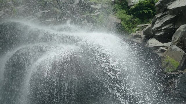 Close up of water stream splashing and falling on large wet rock from waterfall
