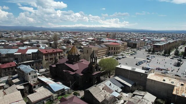 An aerial drone shot of the historic Holy Saviour Church in Gyumri, Armenia, showcasing its unique black tufa stone architecture and the surrounding cityscape on a sunny day.

