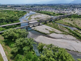 Obraz premium Aerial view of a river flowing through green countryside. Bridge spans the water, connecting towns on either side. Vehicles travel across the bridge, moving steadily forward