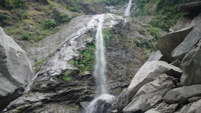 Handheld shot of a tall mountain waterfall flowing down over rocky cliffs