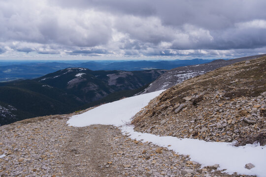 The road through the forest, which is snow-covered in places, leads to a beautiful mountain in the Canadian Rockies 