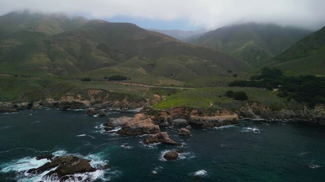 Aerial drone footage of the dramatic coastline at Point Lobos in Big Sur, California. The shot captures rugged cliffs, turquoise Pacific Ocean waves, rocky coves, and untouched natural landscapes.

