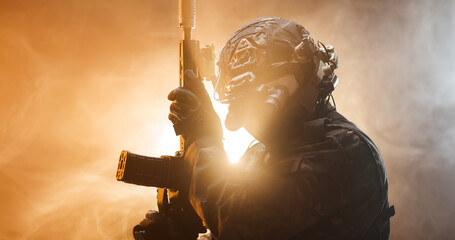 Obraz premium A soldier stands in a low light setting, holding a weapon. Smoke surrounds the soldier, creating a dramatic atmosphere. The scene hints at a mission about to begin