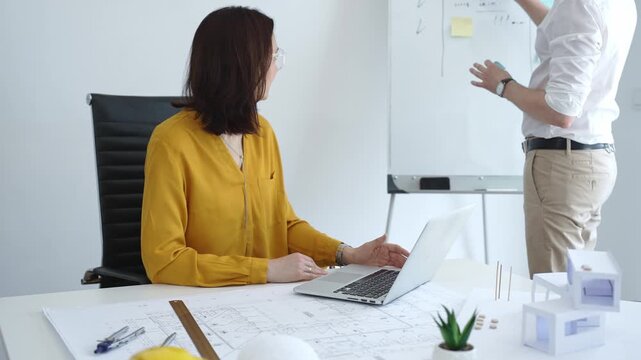 Architects collaborating on modern housing design, analyzing blueprints and scale models, using sticky notes on a whiteboard during a focused planning meeting