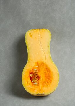 Halved butternut squash (Cucurbita moschata) showing orange flesh and seeds, also known as butternut pumpkin or labu madu, on a gray background.