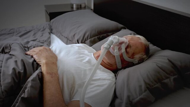 Mature adult sleeping at night while wearing a CPAP mask to treat his Sleep Apnea.