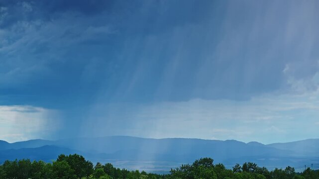 A dramatic rain curtain falling from thunderclouds above distant mountains in Hokkaido, Japan. Dynamic weather scene capturing the power of summer storms and atmospheric conditions.
