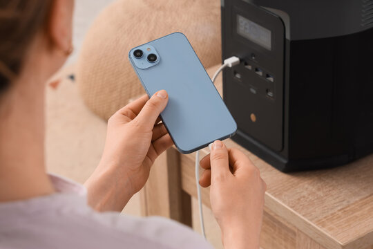 Woman connecting smartphone to portable power station for charging, modern technology and energy solution, this setup provides convenient charging for mobile devices