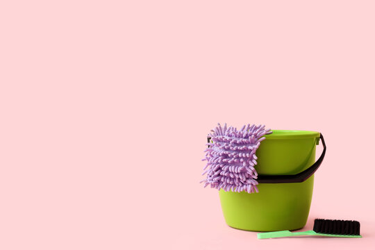Green cleaning bucket with purple microfiber mop and brush on pink background, household chores and sanitation, household chores and sanitation are essential for maintaining a clean environment