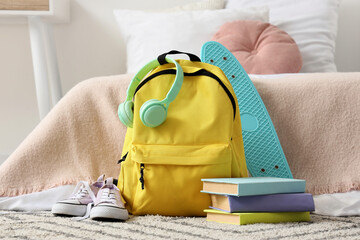 Yellow backpack with mint green headphones, turquoise skateboard, books, and sneakers for school or travel © Pixel-Shot