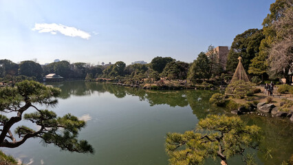 Fototapeta premium Serene Japanese Garden Pond with Traditional Tea House and City Skyline