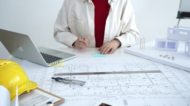 Architect working on new residential project using laptop, reviewing blueprints and drafting floor plans for modern building design with a 3d model on office desk