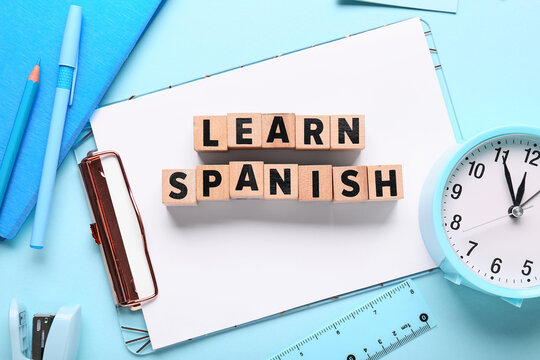 Learn spanish language education with wooden blocks, stationery, and clock on blue background