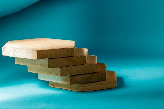 A creative staggered stack of five hexagonal wooden blocks arranged like a staircase or steps on a solid cyan colored background. High Quality Photo