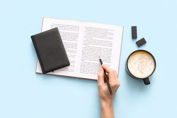Fototapeta premium Female hand with pencil, open book and cup of hot coffee on blue background