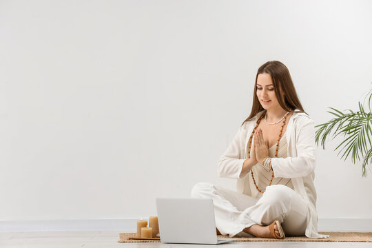 Young woman with laptop meditating near light wall. Zen concept