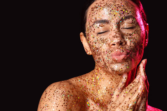 Glamorous woman with glitter makeup and closed eyes posing with kissy face on dark background, the festive and artistic beauty concept is highlighted by the sparkling glitter