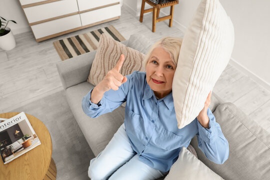 Senior woman with pillow on sofa suffering from loud neighbours at home