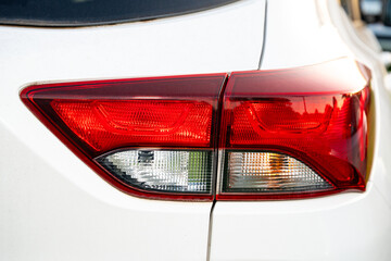 Close-up of a red tail light on a white vehicle, showing reflective plastic, brake light, turn signal, and rear car body detail. © efiederphoto