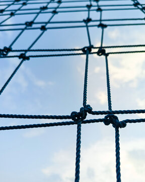 Low angle view of a protective net structure against a blue cloudy sky. The geometric mesh pattern creates strong perspective lines, suitable for concepts related to security, protection, sports facil
